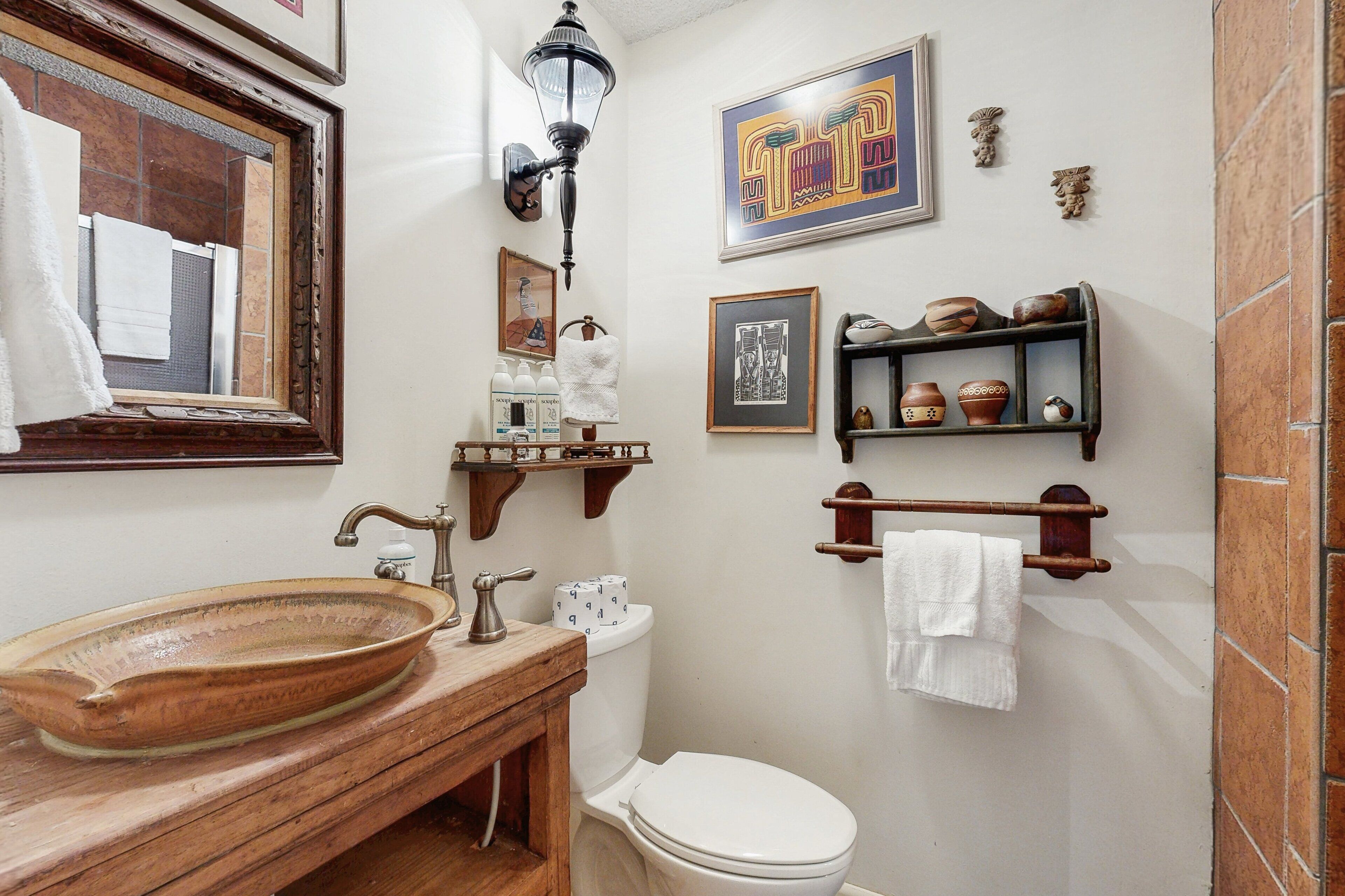 Ein Badezimmer mit einem Holzkosmetikschrank, einem großen Keramikbecken, einer Toilette und einem Regal mit Dekoration.