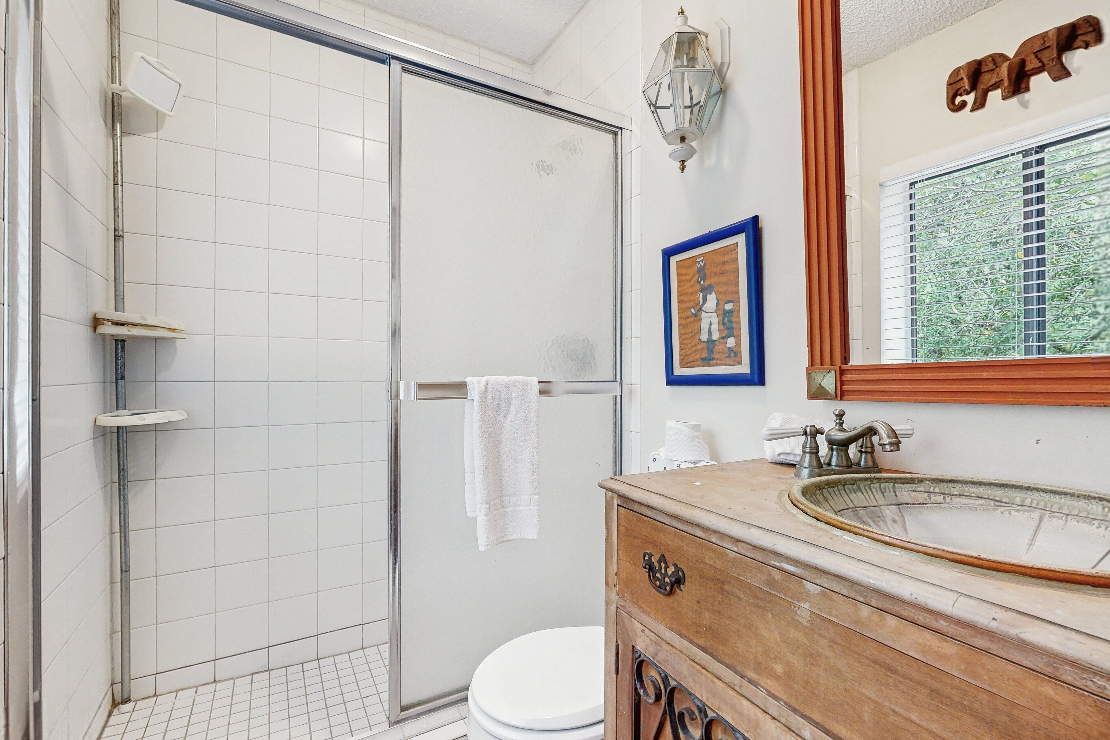 Ein Badezimmer mit einer Duschkabine aus Glas, einer weißen Toilette, einem Holzwaschtisch mit Waschbecken und einem gerahmten Bild an der Wand.