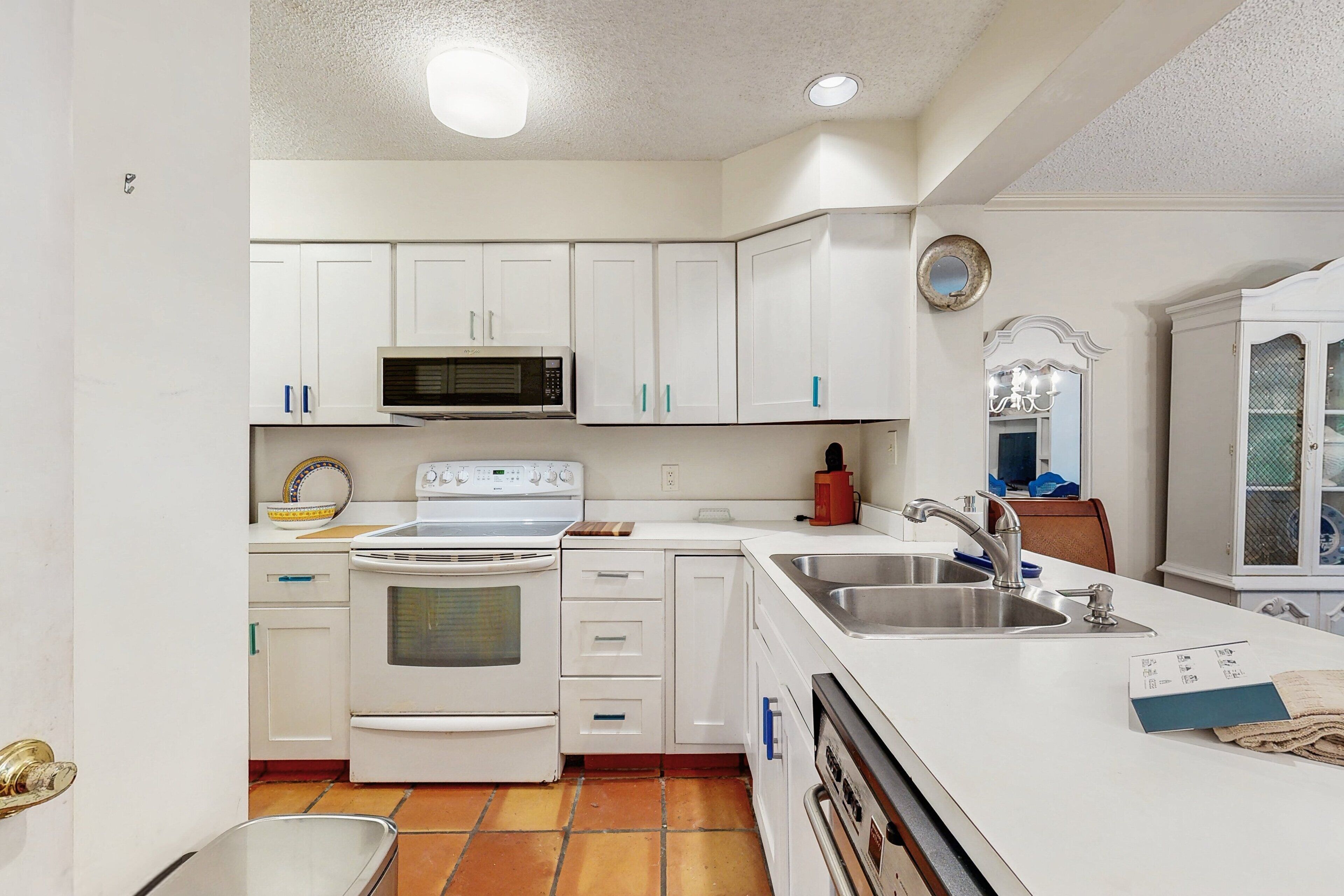 A kitchen with white cabinets, a microwave, stove, sink, and a chandelier.