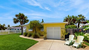 A yellow house with a garage, a white fence, and green lawn. - Spacious Beach House With Private Pool, Firepit and Enclosed Yard (St. Augustine)