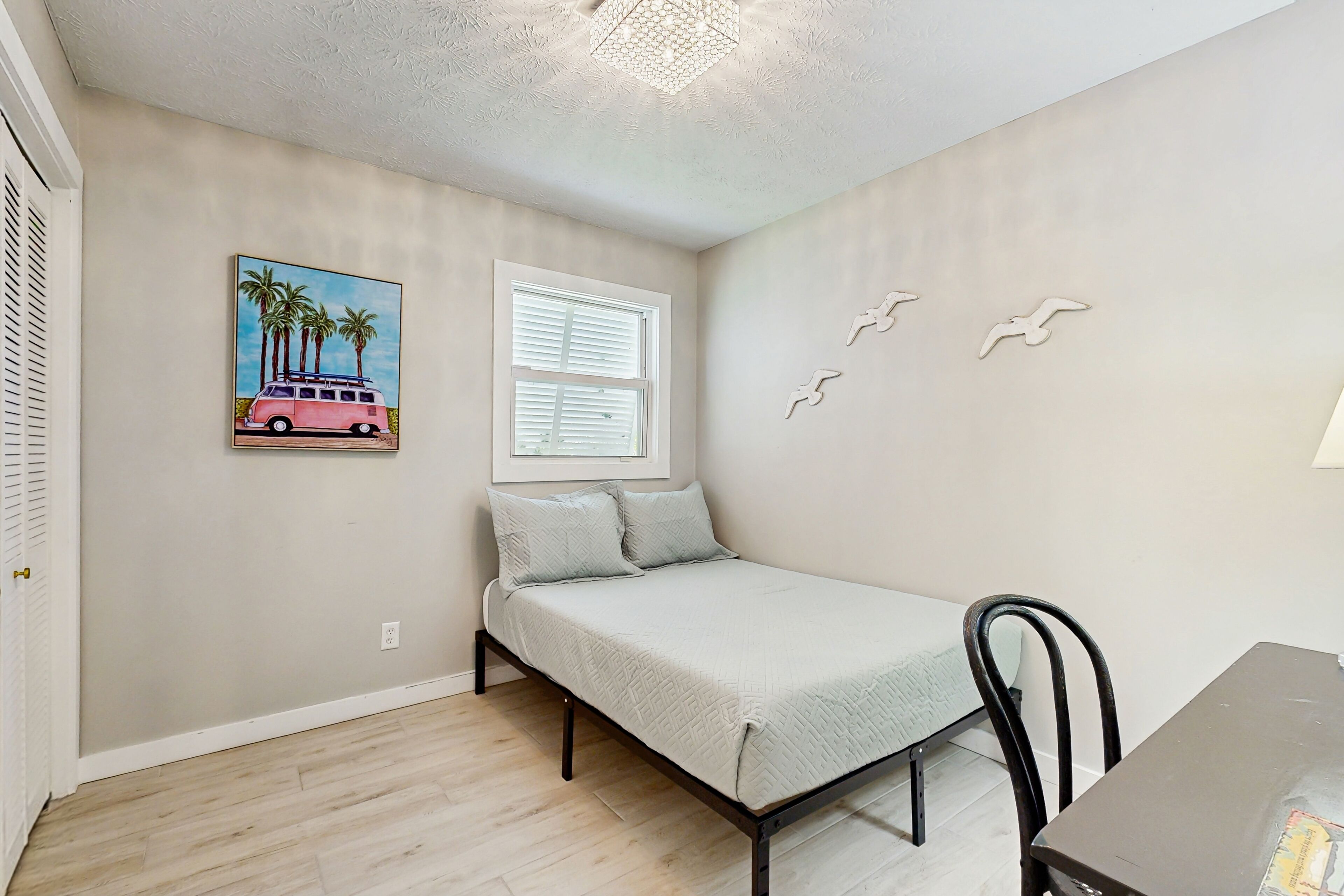 A bedroom with a bed, a window, and a painting of a van on the wall.