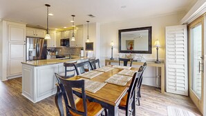 Une cuisine spacieuse avec des meubles blancs, un îlot central en bois et un coin repas comprenant une grande table et des chaises.