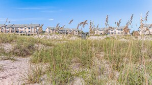 Un hôtel situé en bord de mer, composé de bâtiments à plusieurs étages, entouré de dunes de sable et de hautes herbes.