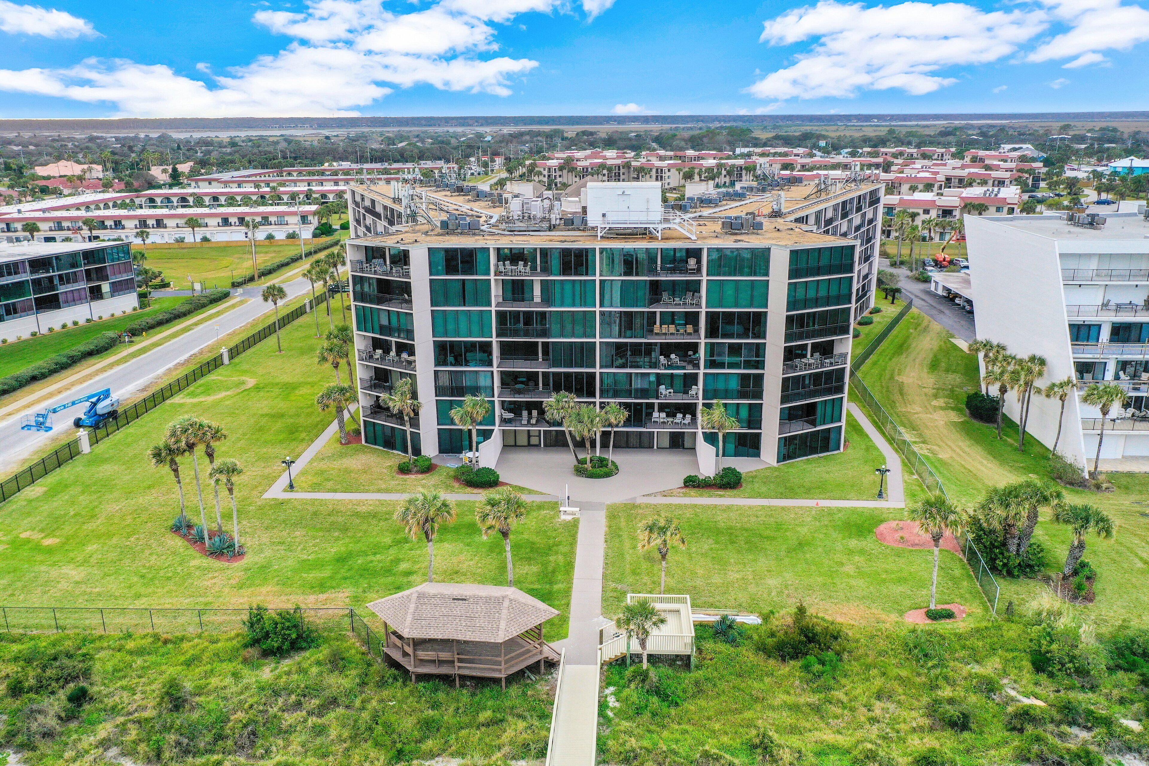 A modern multi-story building with a central courtyard, surrounded by greenery and palm trees.