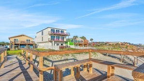 Une promenade en bois menant à des maisons de plage dotées de balcons, sous un ciel dégagé.