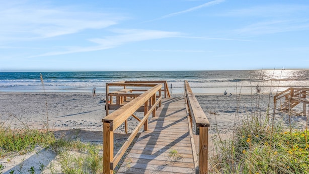 Une promenade en bois qui mène à une plage, avec un ciel dégagé et une mer calme.