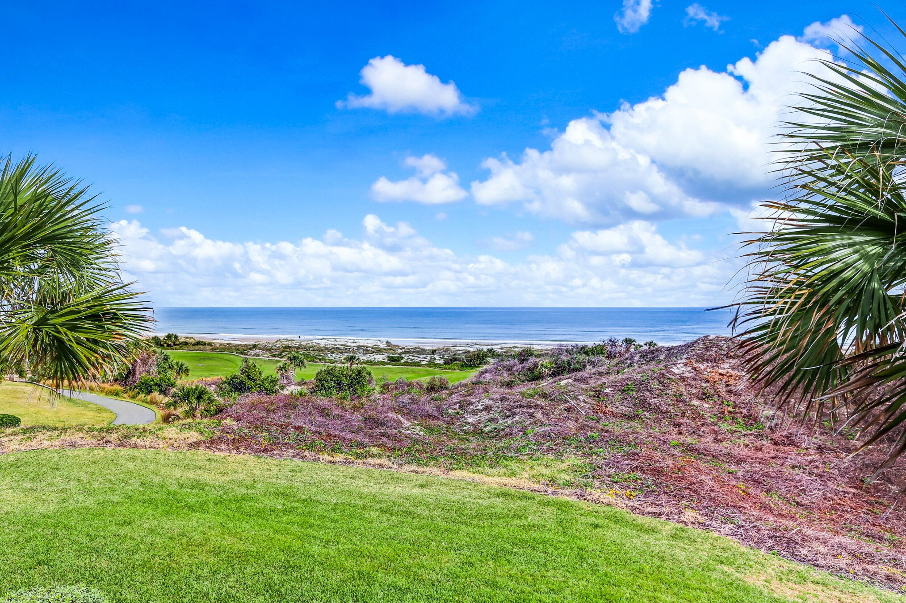 A coastal landscape with a golf course, palm trees, and a view of the ocean.