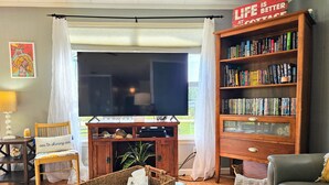 A living room with a flat-screen TV, a bookshelf, a wicker basket, a grey sofa, and a wooden entertainment unit. - Private House Walk to the Beach & Parks! Large Decks, Family Vacation! Hammock Beach (Palm Coast)
