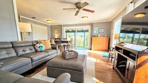 A living room with a sectional sofa, ottoman, wooden cabinet, and a television. - Private House Walk to the Beach & Parks! Large Decks, Family Vacation! Hammock Beach (Palm Coast)