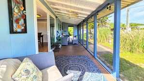 A covered porch with a sofa and cushions, a dining area with chairs, and a view of the surrounding greenery. - Private House Walk to the Beach & Parks! Large Decks, Family Vacation! Hammock Beach (Palm Coast)