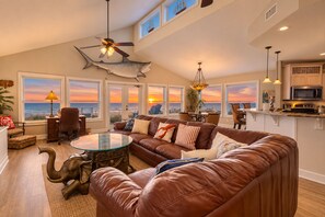 A spacious living room with a large brown leather sofa, a glass coffee table, and a ceiling fan. - Spacious Beachfront Home W/deck, Balcony, Central A/c, Washer/dryer, and Wifi (Fernandina Beach)