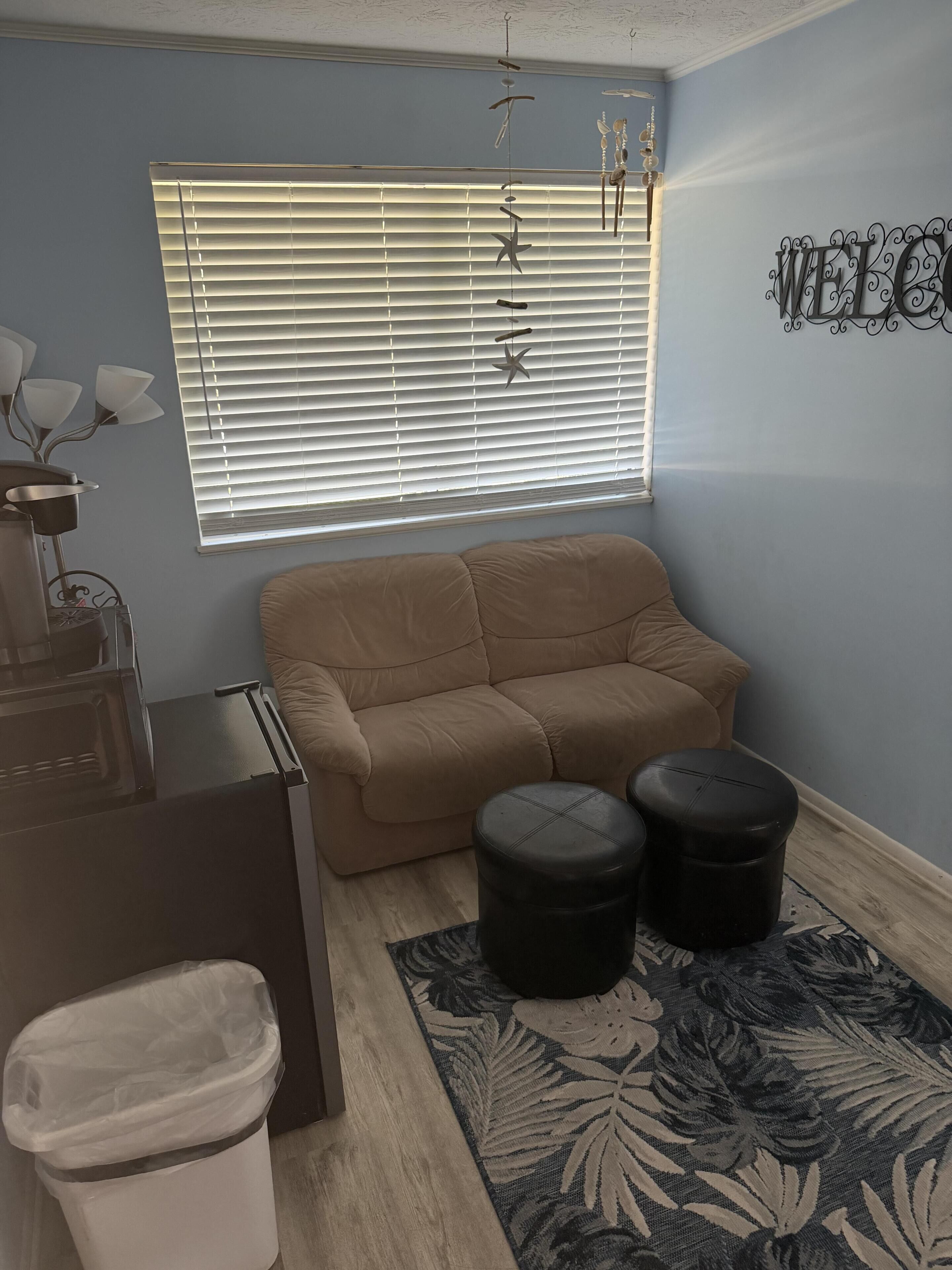 Un soggiorno con un divano beige, due pouf neri, un cestino e un elemento decorativo a parete.