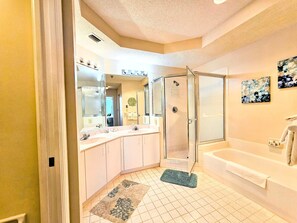 Un baño con ducha, bañera y un espejo grande.