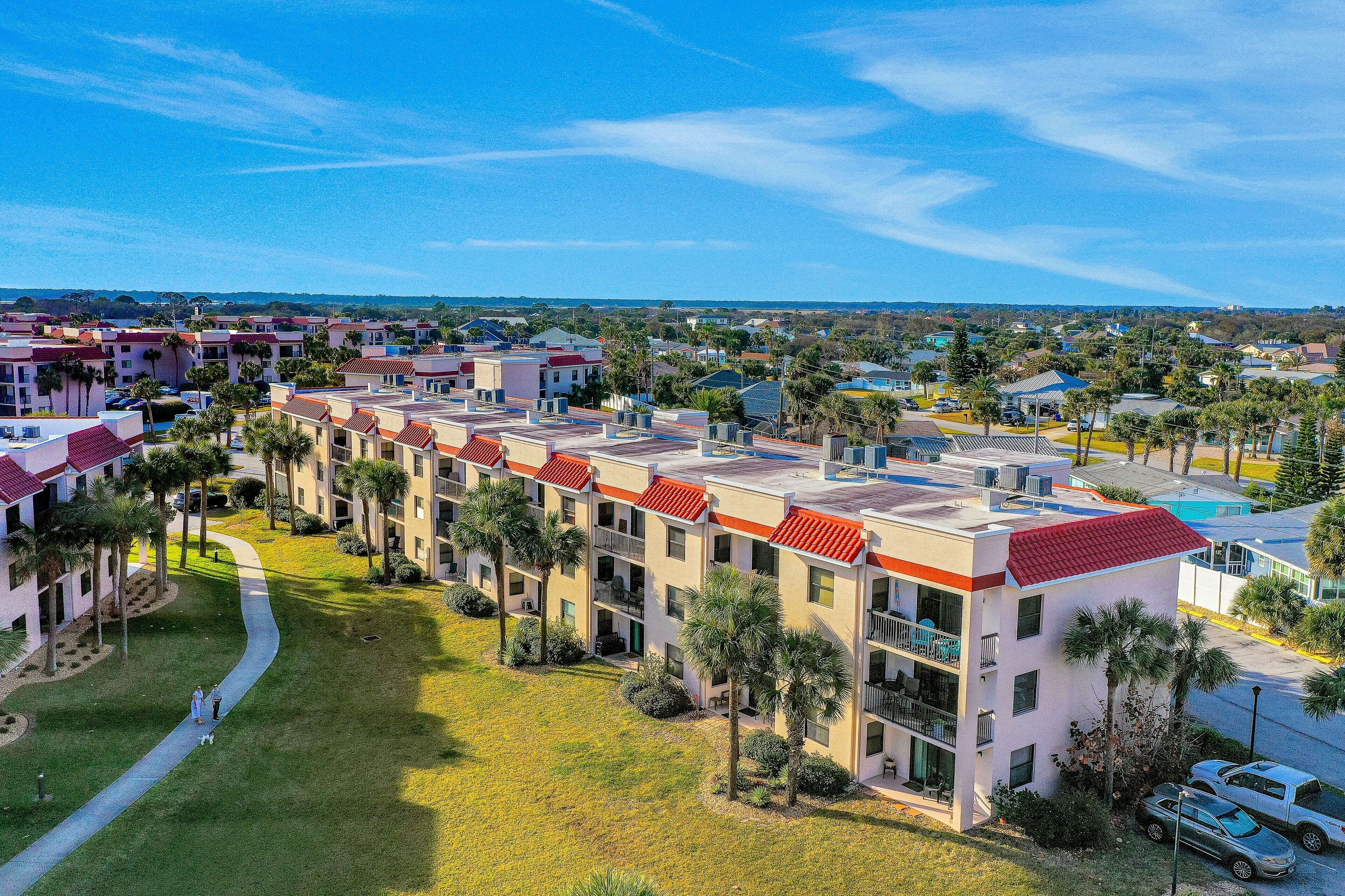 A multi-story hotel with a red-tiled roof, a central courtyard with palm trees, and a view of the surrounding neighborhood.