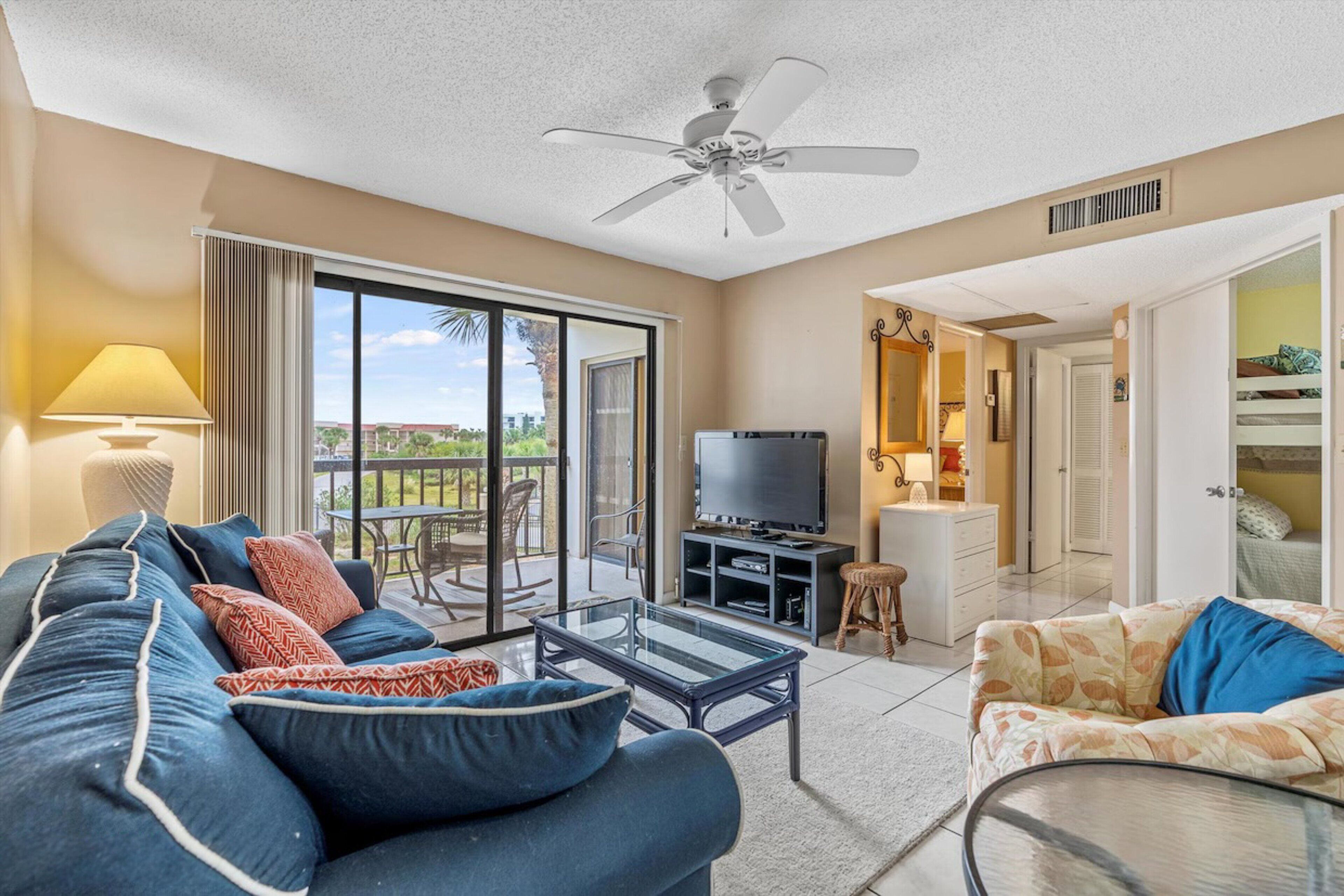 A spacious living room with a large TV, two sofas, a glass coffee table, and a ceiling fan.