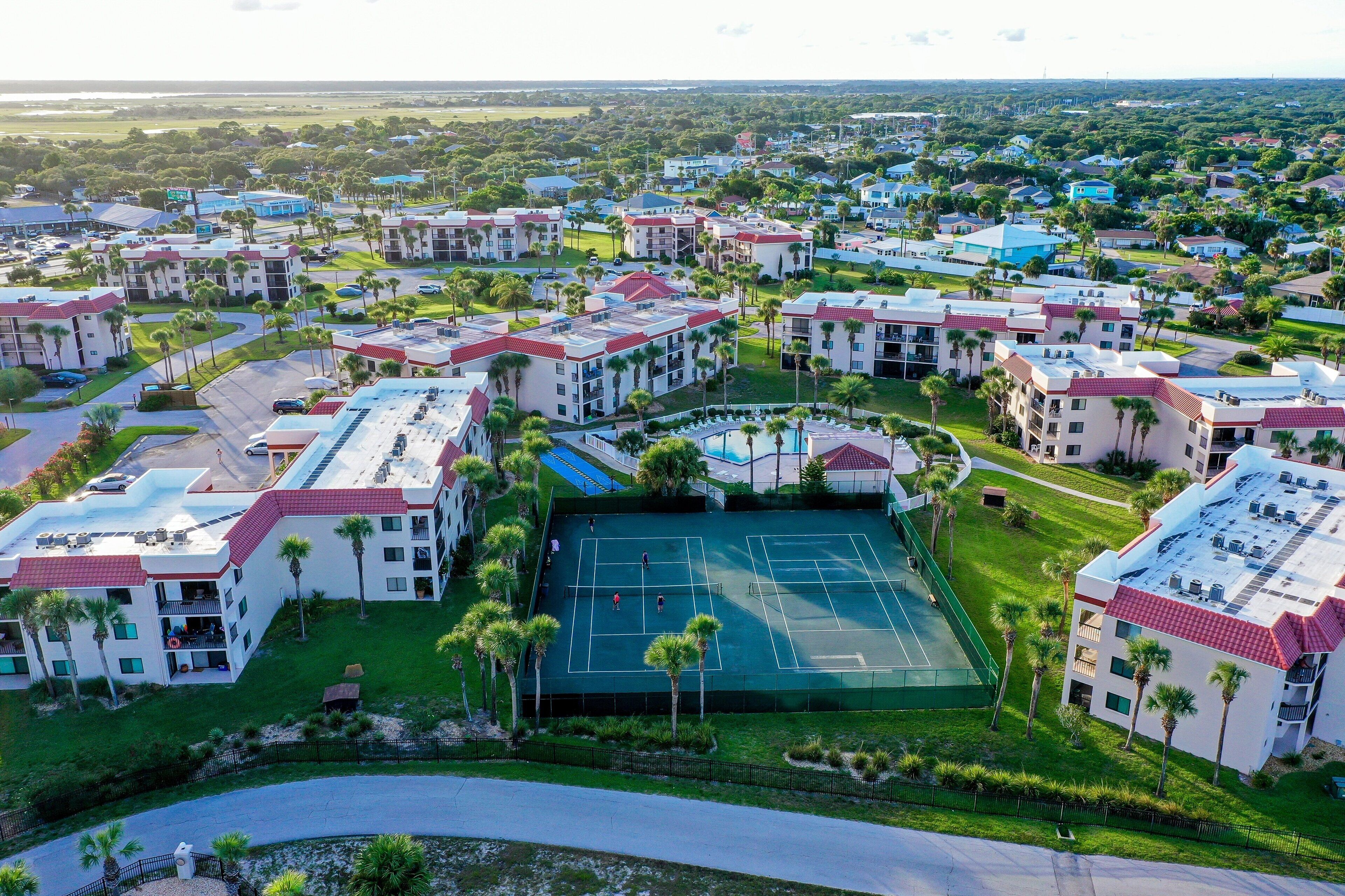 A residential complex with multiple apartment buildings, a tennis court, and surrounding greenery.