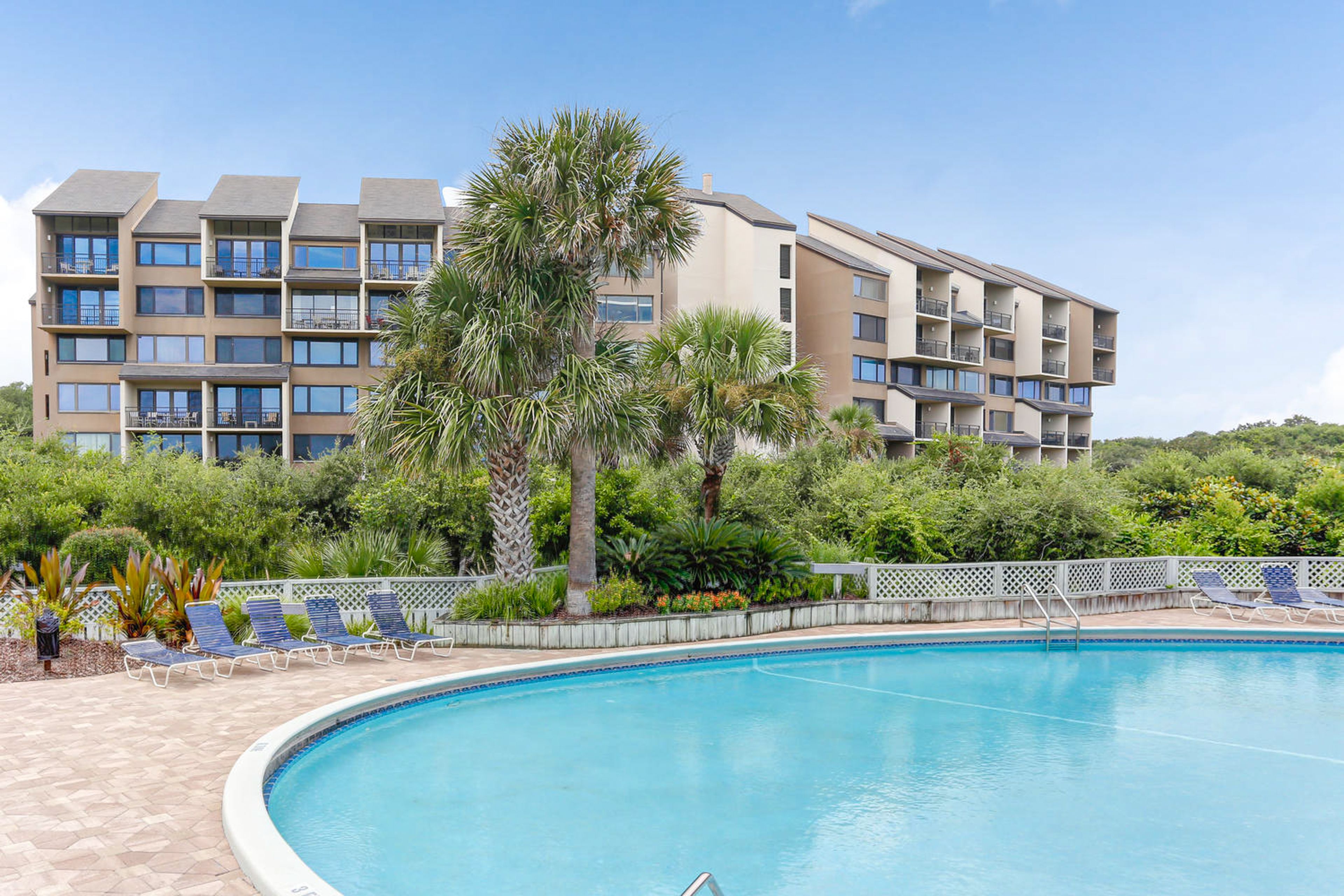 A hotel with a swimming pool, multiple balconies, and lush greenery.