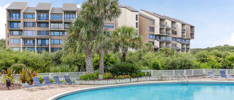 A hotel with a swimming pool, multiple balconies, and lush greenery.