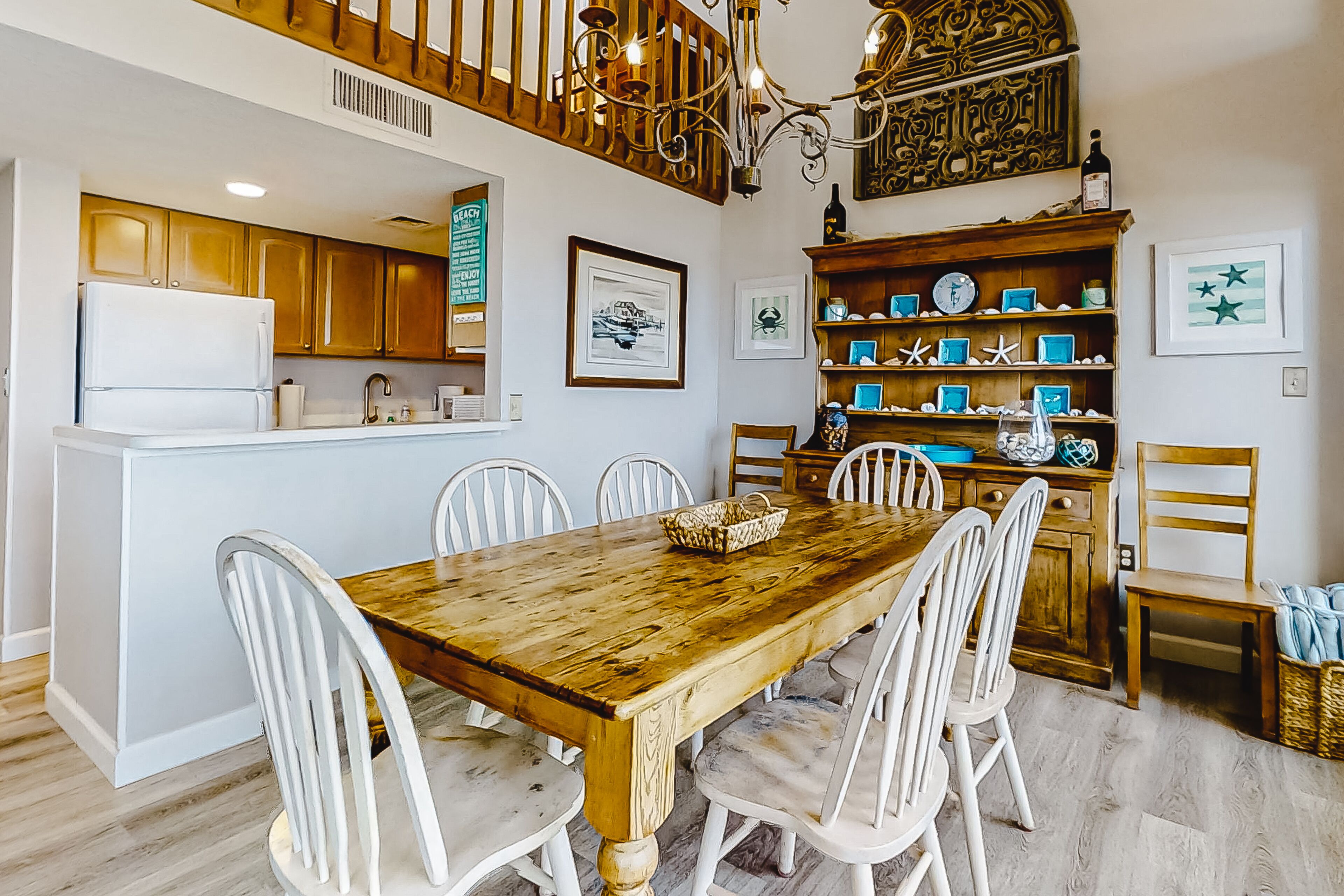 A dining area with a wooden table and white chairs, a kitchen with wooden cabinets, and a chandelier.