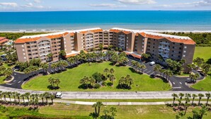 A multi-story hotel with a central courtyard surrounded by palm trees, located near a beach. - Oceanfront Condo,beach Access, Heated Pool, Tennis Courts (Palm Coast)