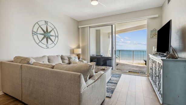 A living room with a beige sofa, a flat-screen TV, and a large window offering a view of the ocean. - Oceanfront Condo,beach Access, Heated Pool, Tennis Courts (Palm Coast)