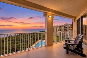 Un balcon avec une piscine, des chaises et une vue sur l’océan au coucher du soleil.