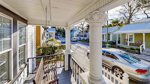 Une véranda avec une balustrade blanche, un banc et une vue sur une rue bordée de voitures et de maisons.