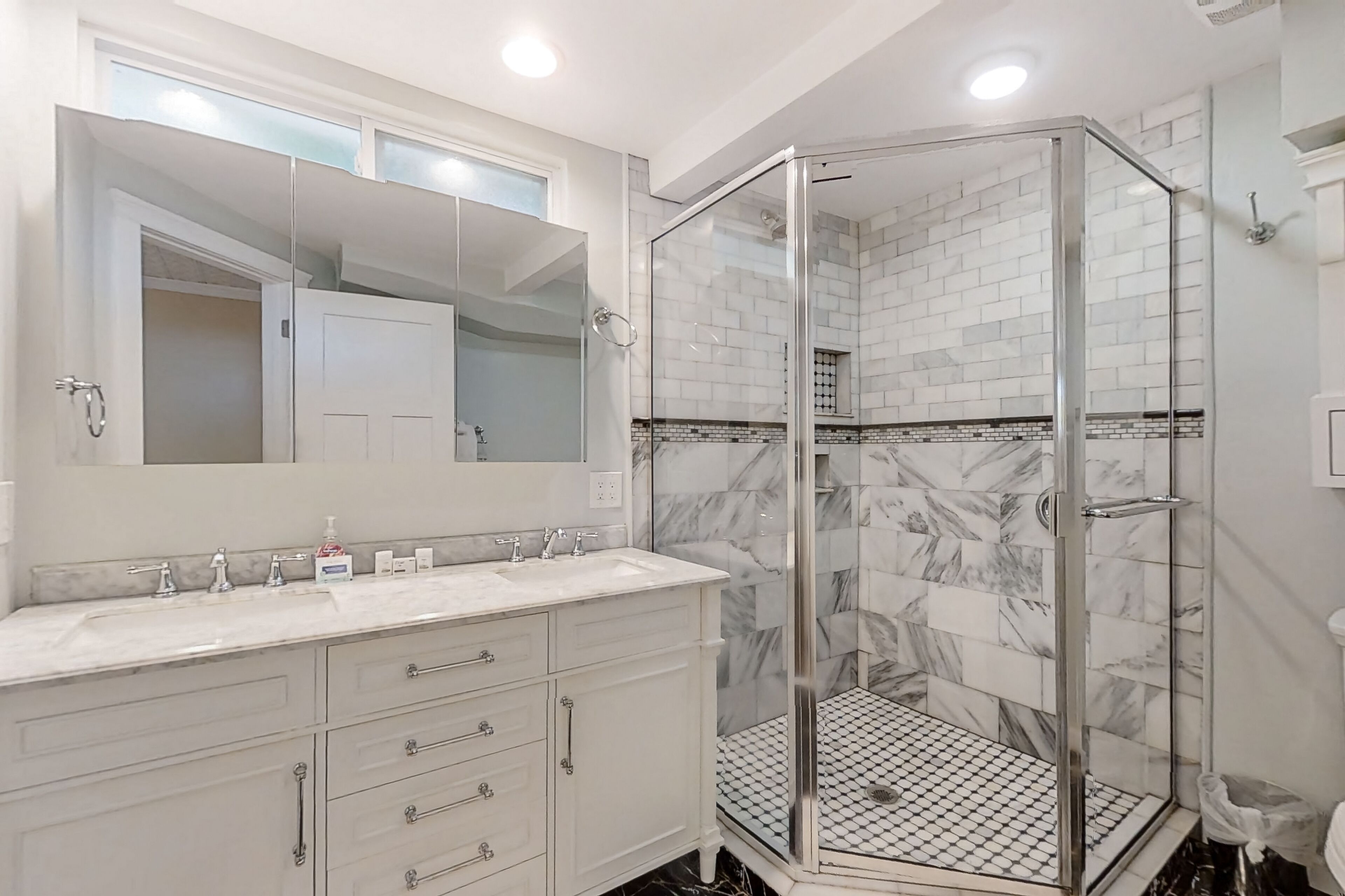 A modern bathroom with a glass-enclosed shower, white marble tiles, and a large mirror above the sink.