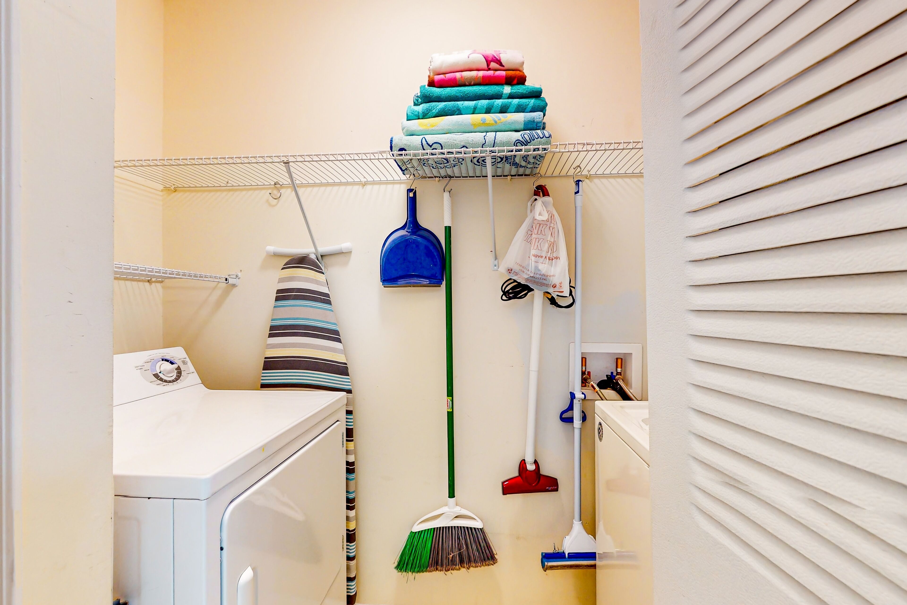 A laundry area with a washing machine, a drying rack, a mop, a broom, and a mop bucket.