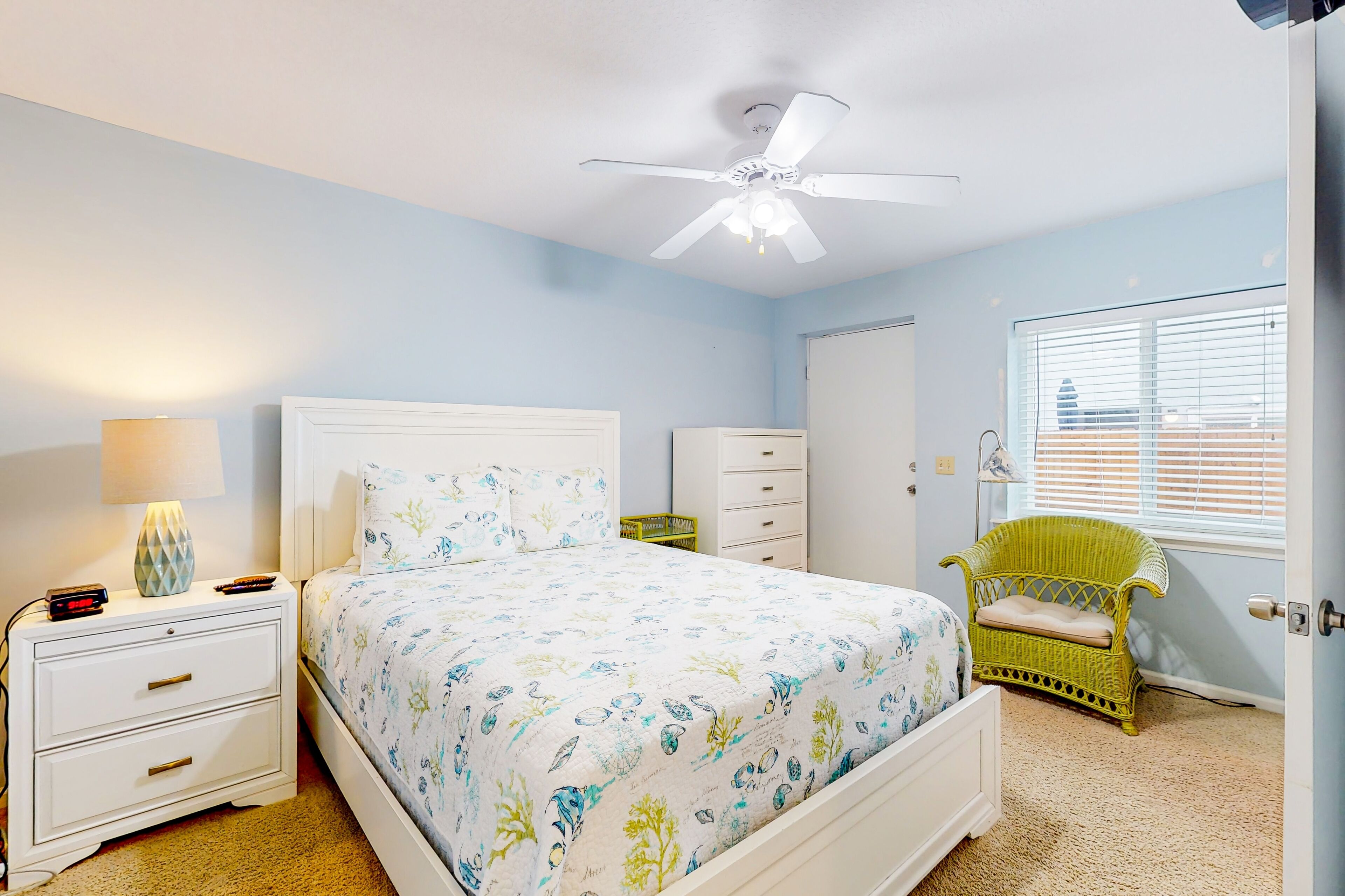 Une chambre à coucher comprenant un lit, une table de chevet, une commode, une chaise et un ventilateur de plafond.