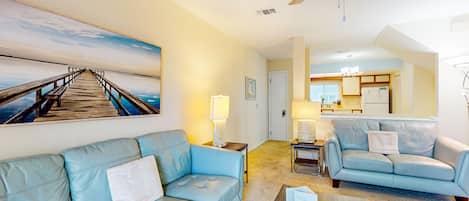 A living room with a blue sofa, a coffee table, and a painting of a pier.