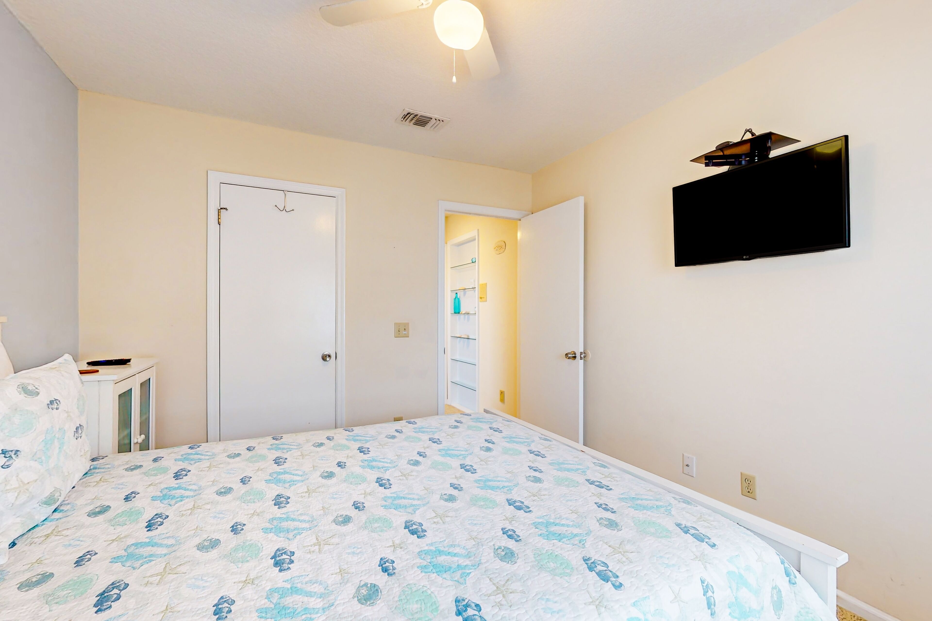 A bedroom with a bed, a television mounted on the wall, and two doors.