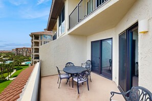 Ein Balkon mit rundem Tisch und Stühlen, einer Schiebetür und Blick auf einen Pool und weitere Gebäude.