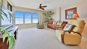 A spacious living room with a large window, a ceiling fan, a sofa, a chair, and a TV. - Sand Dollar III 605 (St. Augustine)