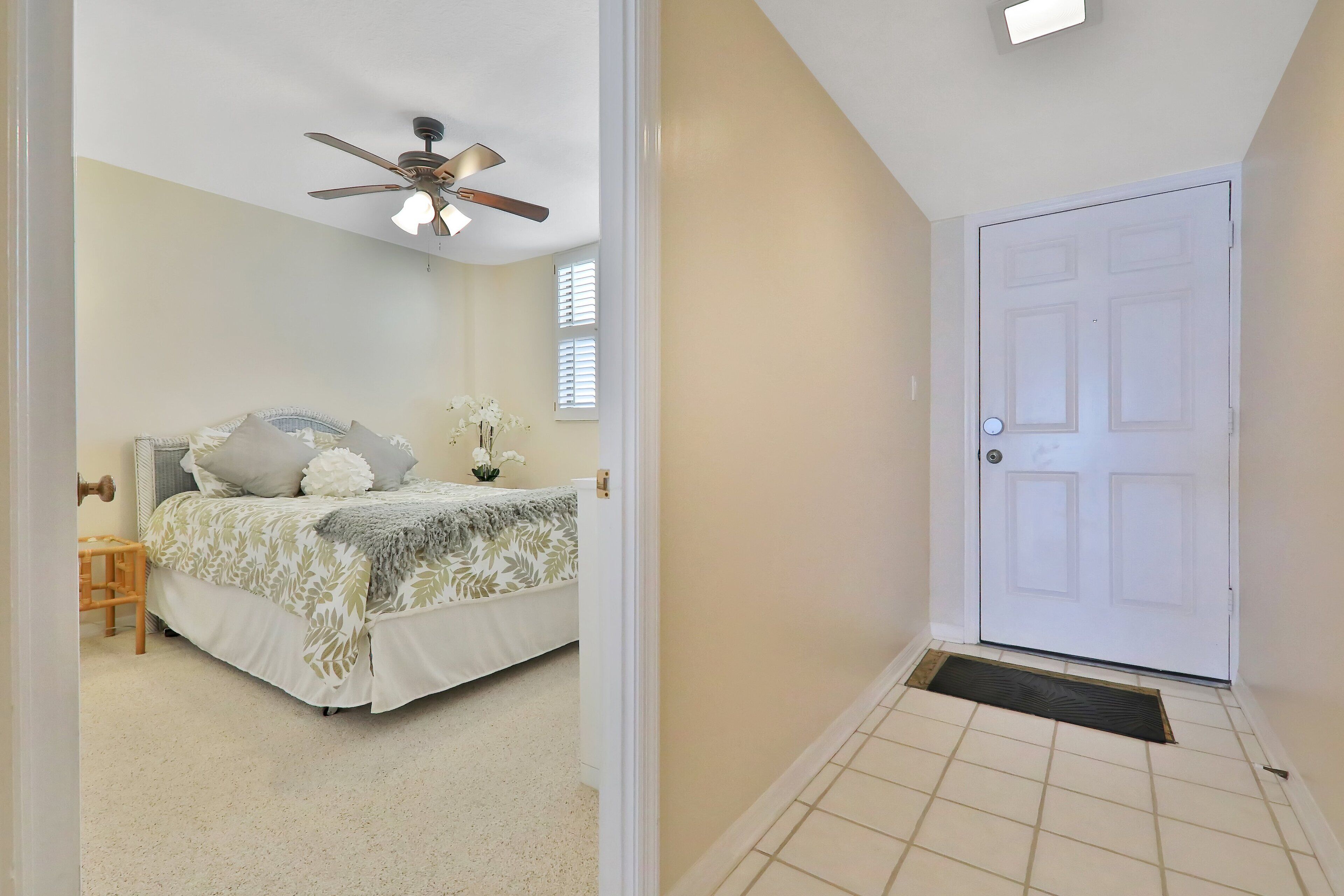 A bedroom with a bed, a ceiling fan, a door, and a window.