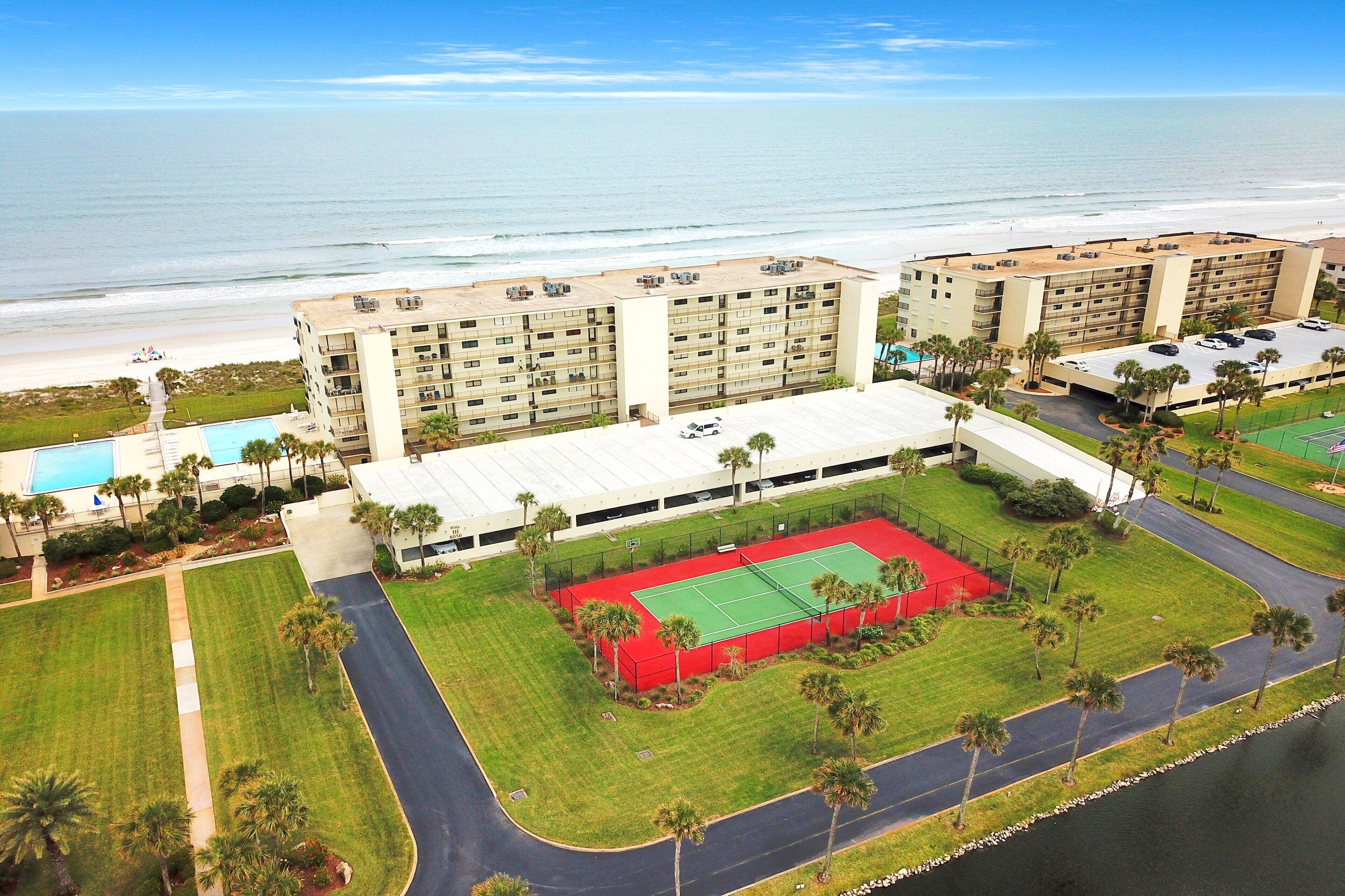 Hotel com vários andares, quadra de tênis, piscina e vista para a praia.
