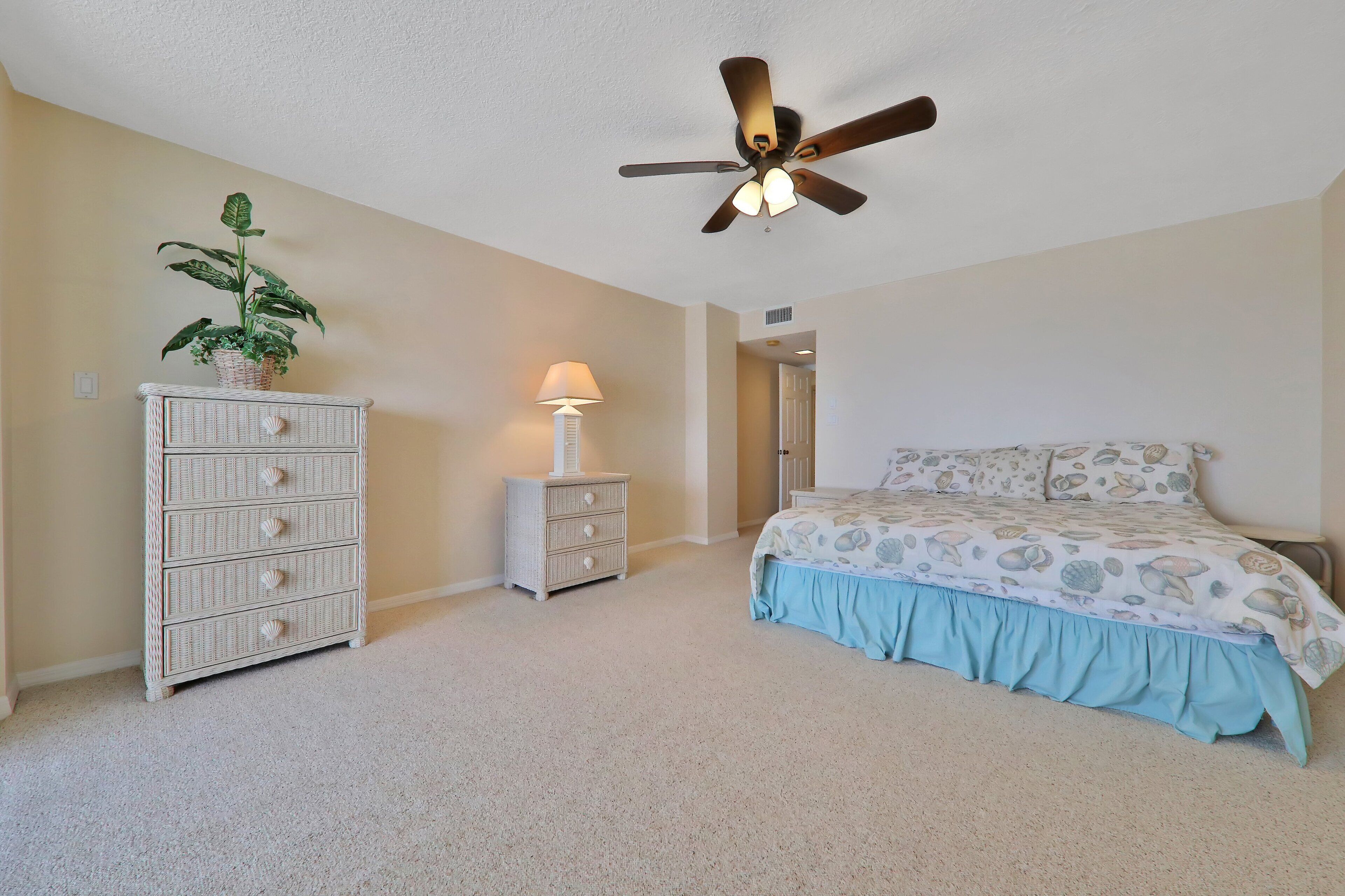 A bedroom with a bed, a dresser, a lamp, and a ceiling fan.
