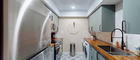 A compact kitchen with stainless steel appliances, a wooden countertop, and a tiled floor.
