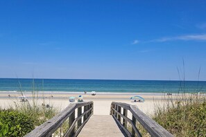 A wooden boardwalk leading to a beach with umbrellas and people. - Spacious Condo With 2 Private Balconies, Beach Access and Pool (St. Augustine)