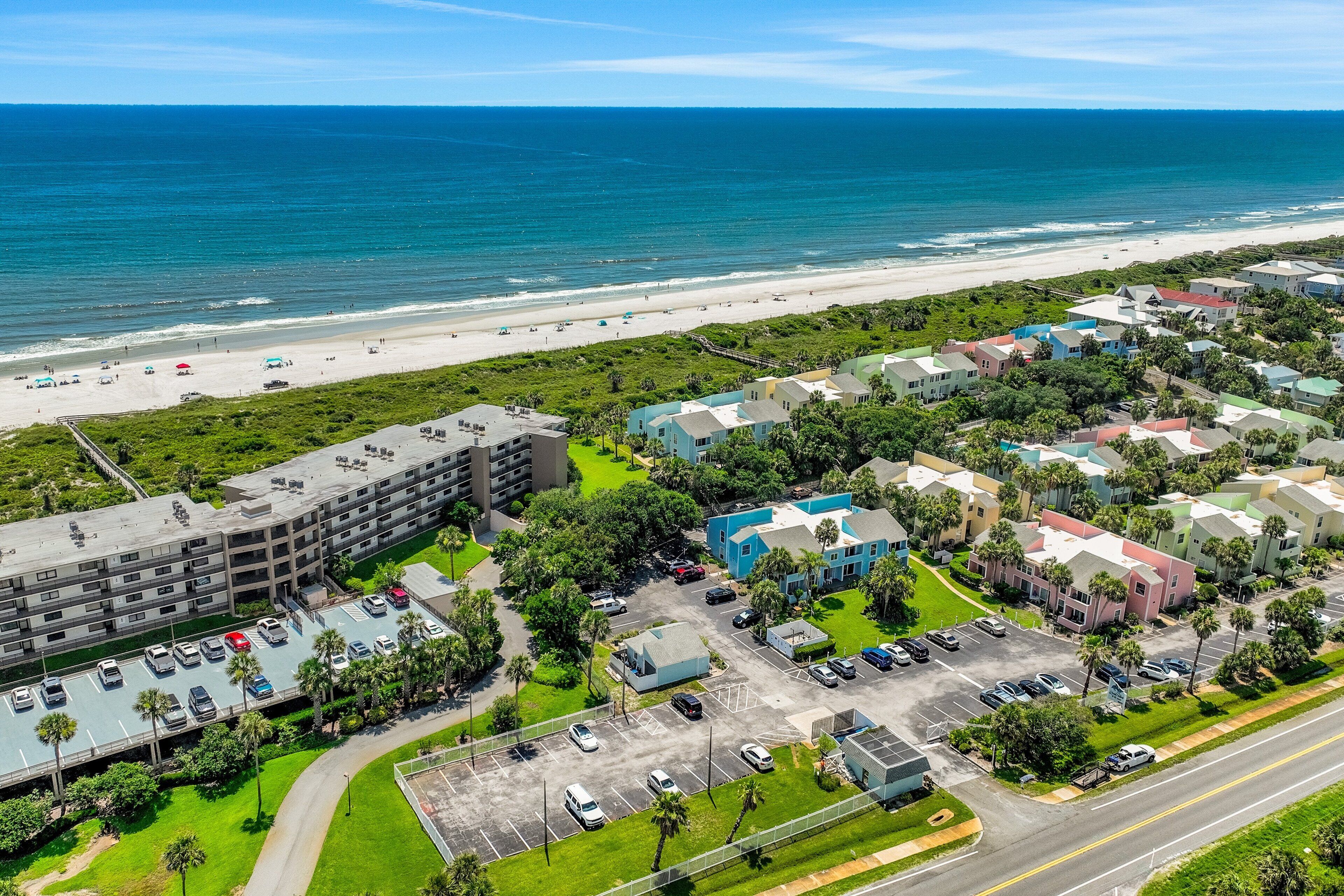 An aerial view of a coastal hotel with multiple buildings, parking areas, and a beach in the background.