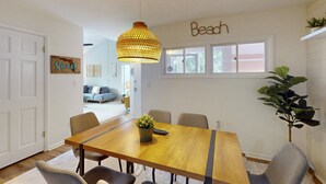 Ruokailutilassa on puinen pöytä, tuolit, riippuvalaisin ja seinässä oleva kyltti, jossa lukee ”Beach”.