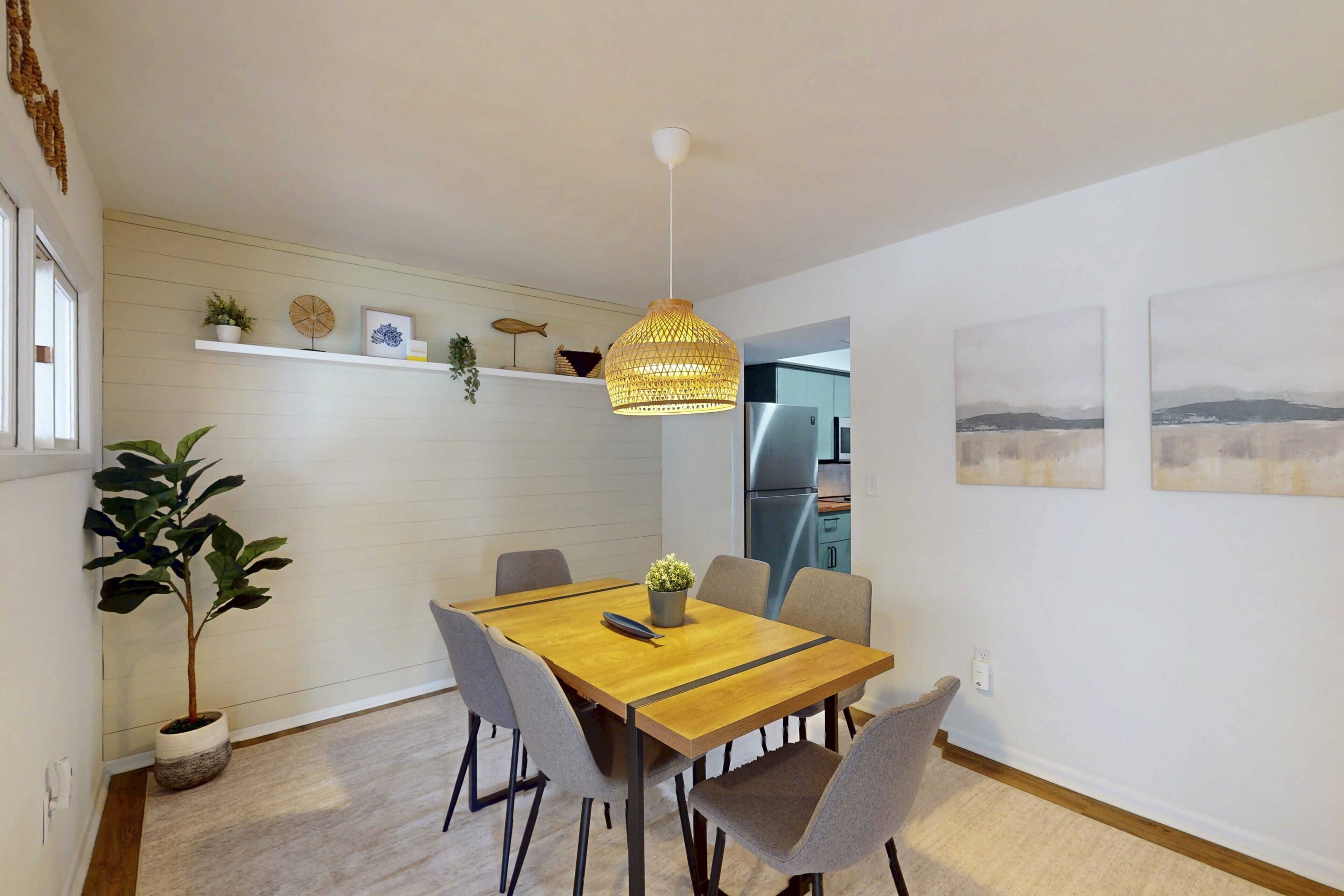 Ein Essbereich mit Holztisch, grauen Stühlen, einer Hängelampe und einem Blumentopf.