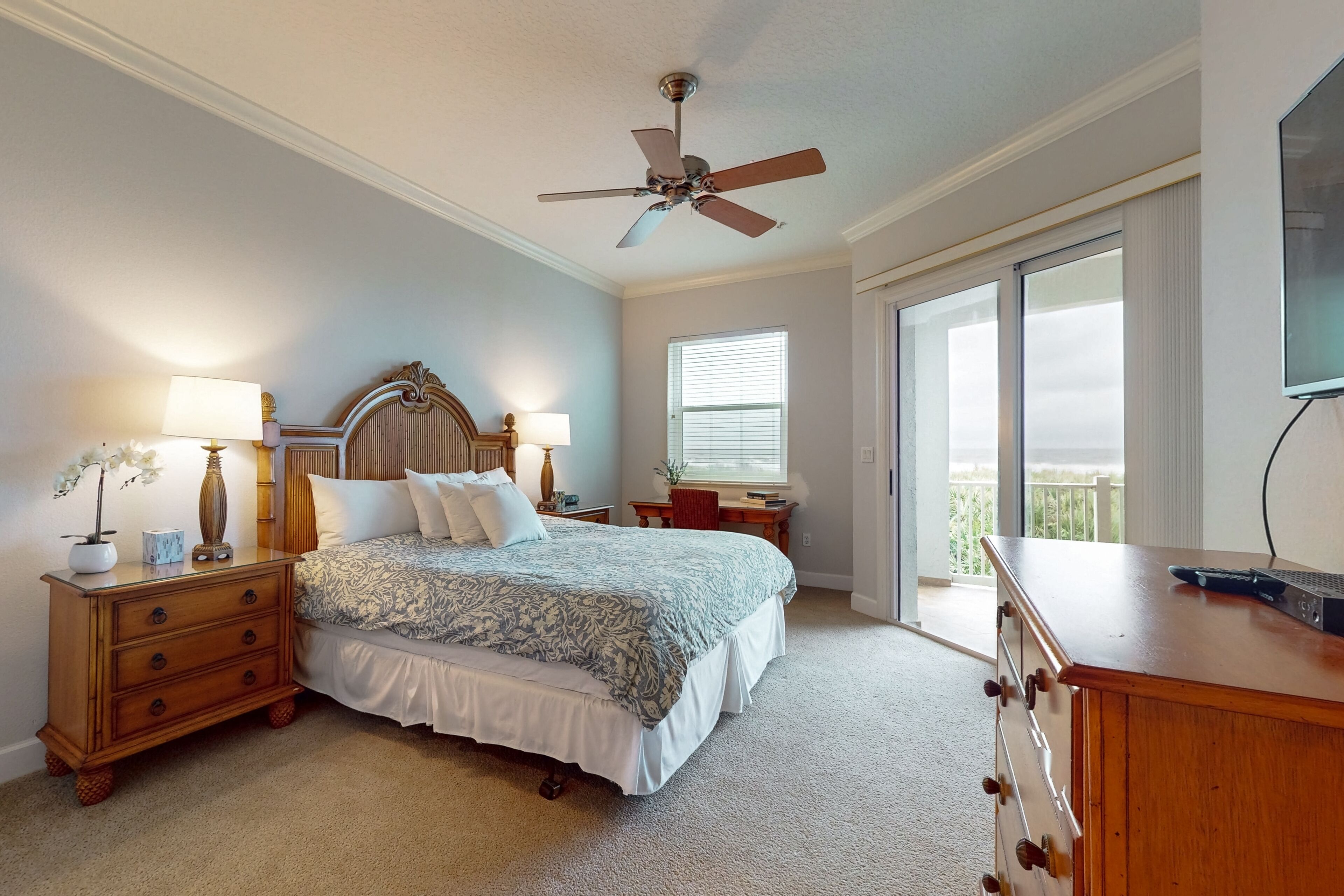 A bedroom with a bed, nightstands, a dresser, a ceiling fan, a window, and a TV.