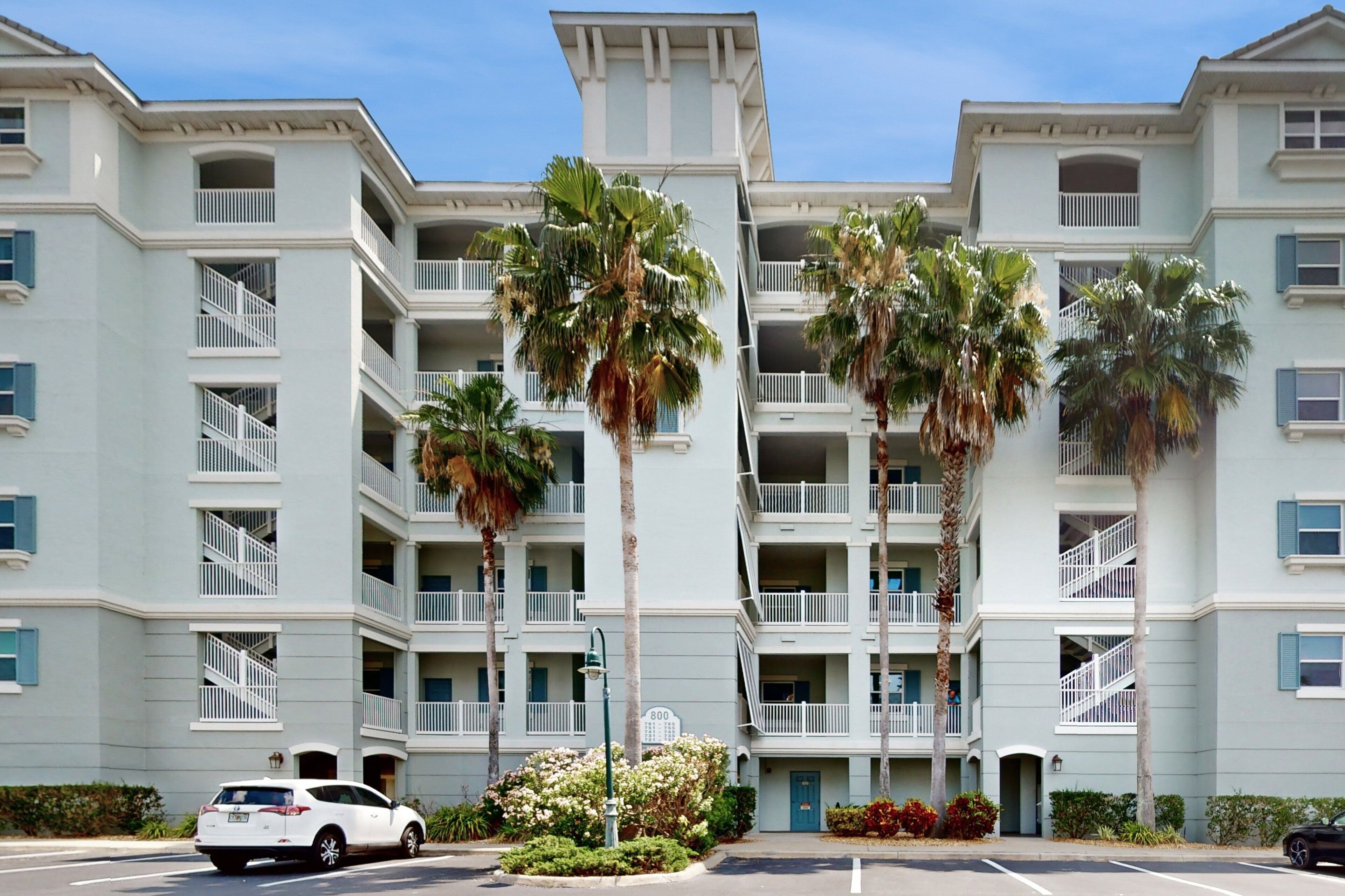 A multi-story hotel with balconies, palm trees, and a parking lot.