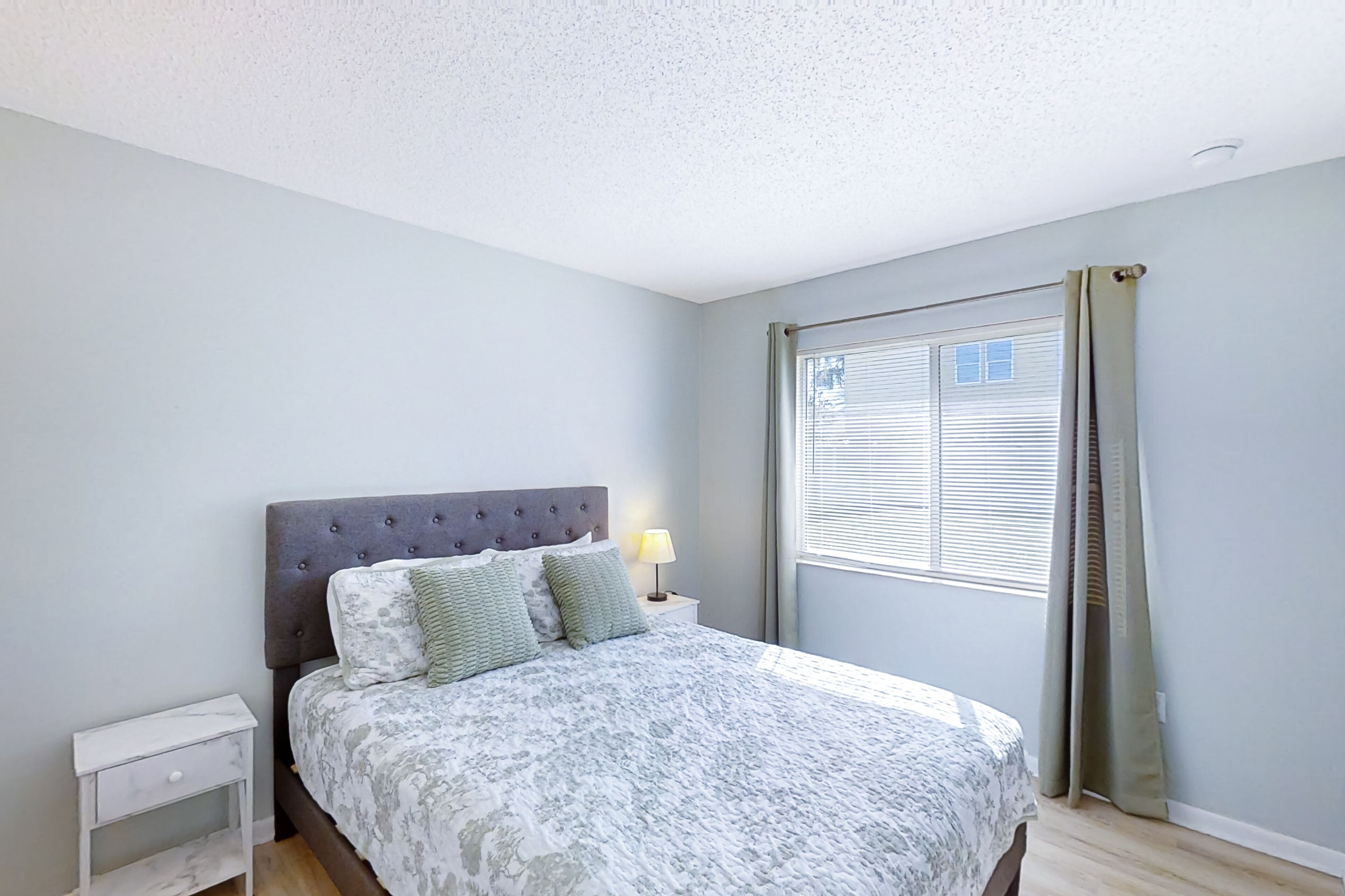 A bedroom with a bed, nightstand, and window with curtains.