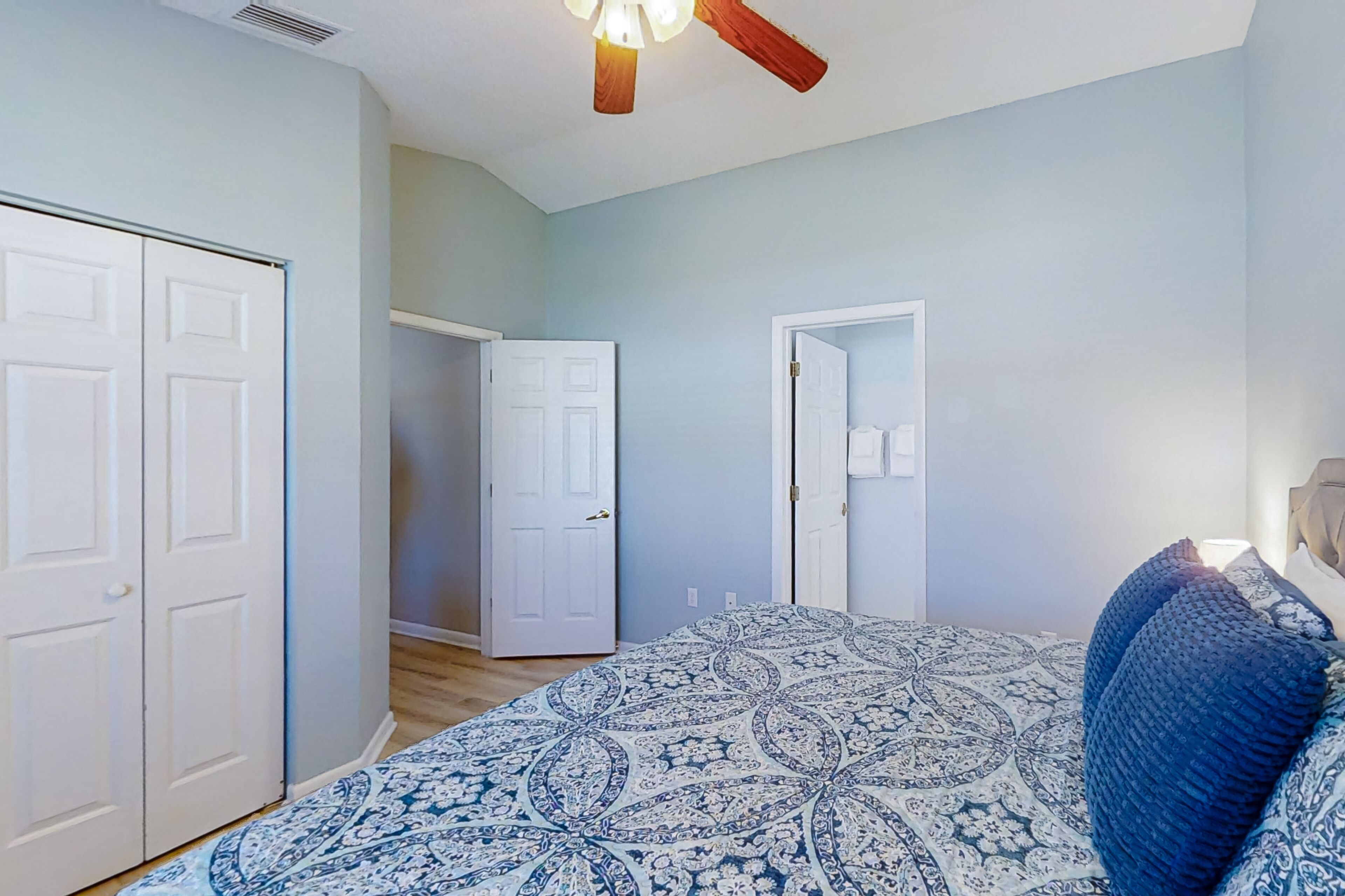 A bedroom with a bed, a ceiling fan, and two doors leading to other rooms.