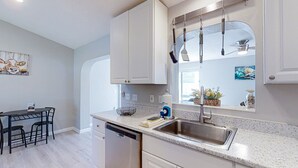A modern kitchen with white cabinetry, a stainless steel sink, and a dining area with a black metal table and chairs. - Pristine Palms House in Palm Coast With Enclosed Pool & Full Kitchen (Palm Coast)