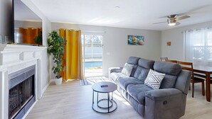 A living room with a fireplace, sofa, coffee table, and a dining area with a table and chairs. - Pristine Palms House in Palm Coast With Enclosed Pool & Full Kitchen (Palm Coast)