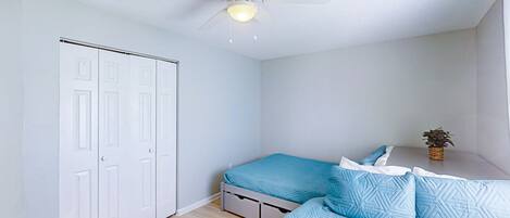 A bedroom with a bed, a ceiling fan, a wardrobe, and a small table with a plant.