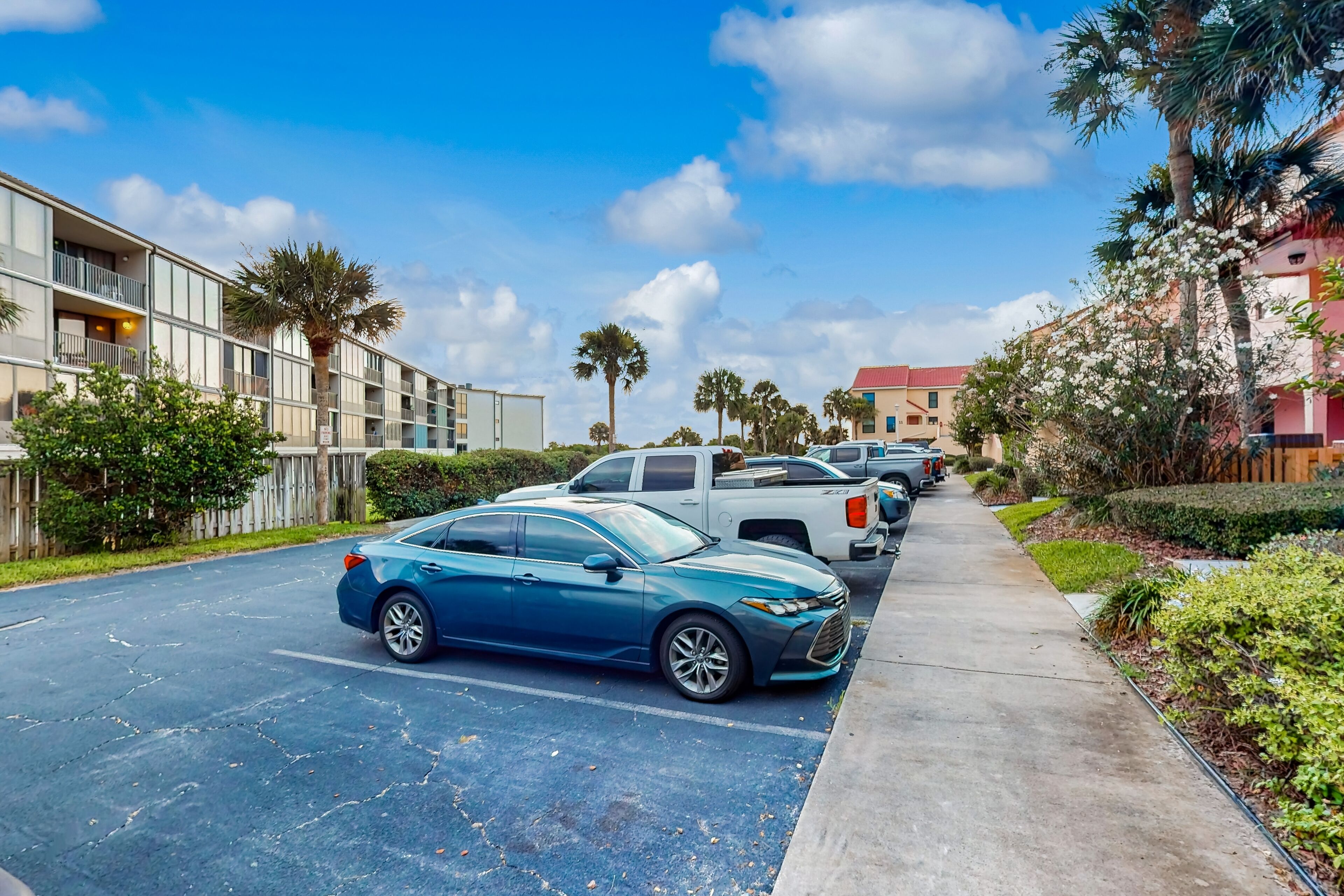 A parking lot with a blue car, a white truck, and a row of parked cars.